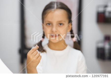 Portrait of young Caucasian girl displaying freshly lost tooth with delight in bathroom. Symbolizes childhood milestones, growth, and personal achievement. Portrait of young Caucasian girl displaying freshly lost tooth with delight in bathroom. Symbolizes childhood milestones, growth, and personal achievement. 120977391