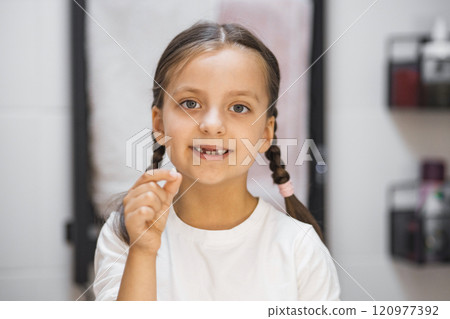 Portrait of young Caucasian girl holding baby tooth, smiling into bathroom mirror. Celebrating milestone of losing first tooth with happiness and curiosity. Bright eyes and braided hair. Portrait of young Caucasian girl holding baby tooth, smiling into bathroom mirror. Celebrating milestone of losing first tooth with happiness and curiosity. Bright eyes and braided hair. 120977392