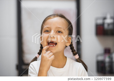 Little Caucasian girl with missing baby teeth examining her reflection in bathroom mirror. Joyful moment of childhood captured with focus on dental development. Little Caucasian girl with missing baby teeth examining her reflection in bathroom mirror. Joyful moment of childhood captured with focus on dental development. 120977399