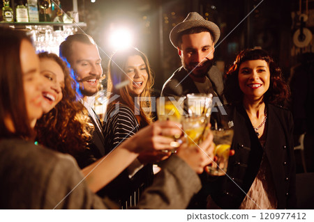 Cheering and drinking cocktails. Group of friends partying in nightclub, toasting drinks cocktails. 120977412