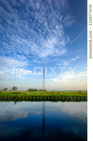 A serene landscape with a stunning reflection and an impressive tower under a cloudy sky 120977439