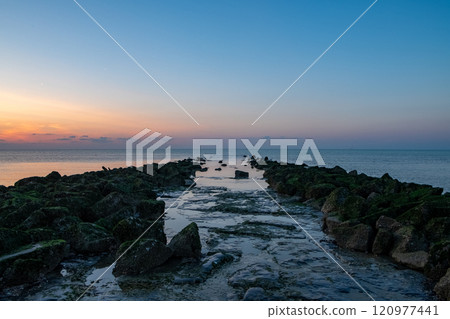 Experience the serene and breathtaking sunset occurring over the rocky jetty at dawn 120977441