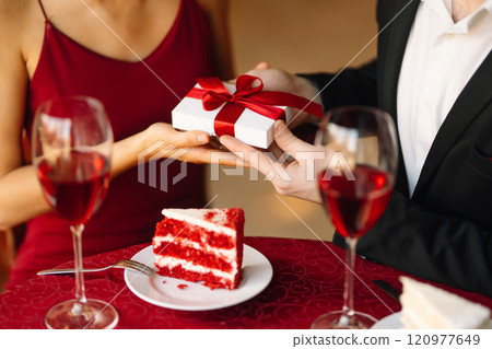 Couple in love exchanges gifts. Handsome man and woman on a date in a restaurant. Concept of love. Couple in love exchanges gifts. Handsome man and woman on a date in a restaurant. Concept of love. 120977649