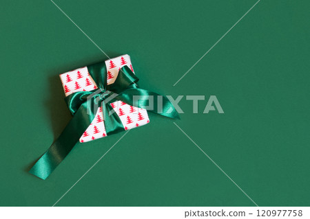Christmas creative white gift box with green bow on green background. Xmas Holiday card. View from above. Copy space. Christmas creative white gift box with green bow on green background. Xmas Holiday card. View from above. Copy space. 120977758