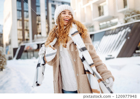Smiling woman in a scarf and hat is having fun at street holiday fair, drinking hot drink. 120977948