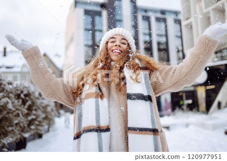 Smiling woman in a scarf and hat is having fun at street holiday fair, drinking hot drink. Smiling woman in a scarf and hat is having fun at street holiday fair, drinking hot drink. 120977951
