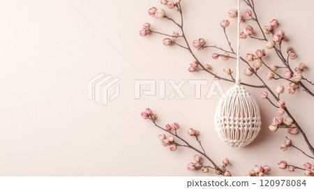 A macrame egg with wooden beads and dried flowers hangs beautifully on a soft beige tablecloth, showcasing Easter charm 120978084