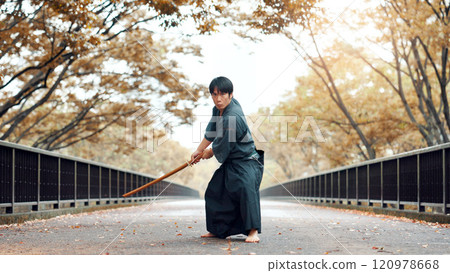 Martial arts, man and wood sword outdoor with fight, battle and samurai training on road. Park, urban and challenge with bamboo weapon, kendo and warrior in autumn in Japan with forest and fighter 120978668