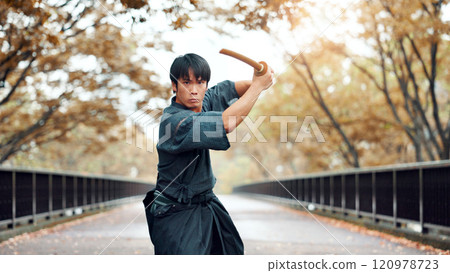 Martial arts, man and wood sword with fight, battle and samurai training on road. Park, urban and challenge with bamboo weapon, kendo and warrior in autumn in Japan with forest and fighter outdoor 120978723