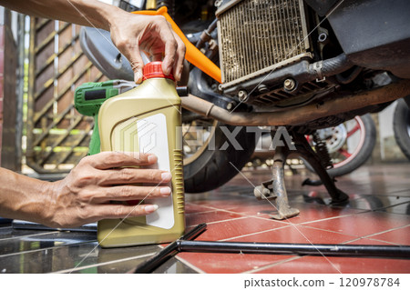 Motorcycle mechanic change the motorcycle oil engine at garage Motorcycle mechanic change the motorcycle oil engine at garage 120978784