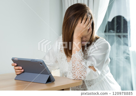 An Asian woman experiences eye strain and fatigue while reading her work schedule on a tablet. 120978885