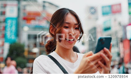 Woman, phone and happy with travel in city, reading and check notification with chat, laugh or meme in street. Girl, smartphone and outdoor on metro sidewalk, smile and app for social media in Japan Woman, phone and happy with travel in city, reading and check notification with chat, laugh or meme in street. Girl, smartphone and outdoor on metro sidewalk, smile and app for social media in Japan 120978934