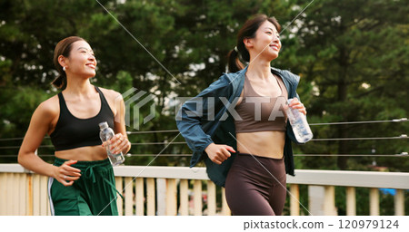 Outdoor, women and smile as friends for running with water bottle for fitness, workout and exercise in Japan. People, city and happy with support for health, self care and wellness with jogging 120979124