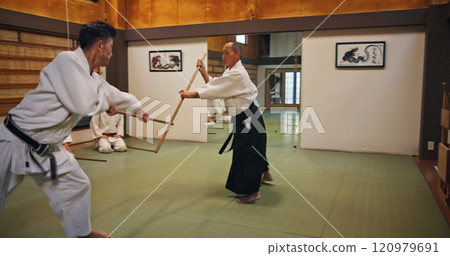 Dojo, class and teacher at Aikido training in gym with wood sword Japanese martial arts and fight exercise in wellness studio. Learning, sport and weapon with people and strike practice for defence 120979691