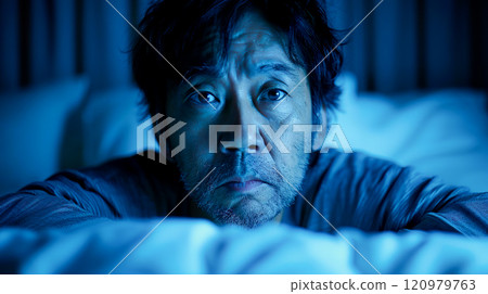 A middle-aged man worried on his bed in a dark room 120979763