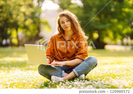 Young curly woman in the park on a green lawn with a laptop in her hands. Online education. Young curly woman in the park on a green lawn with a laptop in her hands. Online education. 120980572