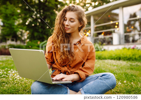 Young curly woman in the park on a green lawn with a laptop in her hands. Online education. Young curly woman in the park on a green lawn with a laptop in her hands. Online education. 120980586