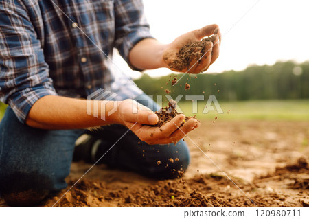Soil is in the strong hands of a farmer on a black field. Agriculture or gardening concept. 120980711