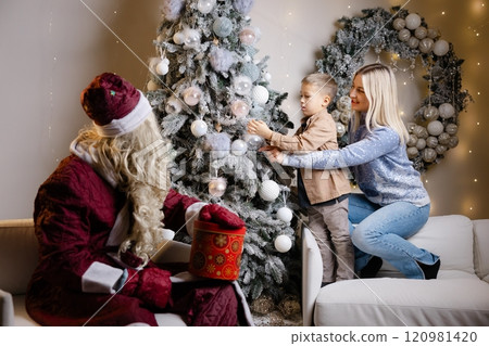 Santa claus watching mother and son decorating christmas tree Santa claus watching mother and son decorating christmas tree 120981420
