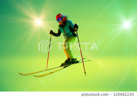 Professional female skier in motion, confident move under neon bright lights against green gradient studio background. Professional female skier in motion, confident move under neon bright lights against green gradient studio background. 120982220