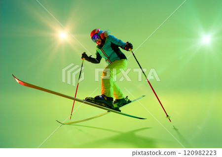 Freestyle skier mid-air, executing dynamic jump with bent knees and balanced posture, dressed vibrant gear against glowing studio background. Freestyle skier mid-air, executing dynamic jump with bent knees and balanced posture, dressed vibrant gear against glowing studio background. 120982223
