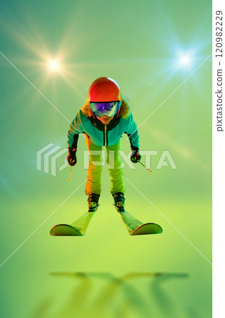Ski enthusiast in mid-air jump in colorful gear against gradient green background with light beams above. Ski enthusiast in mid-air jump in colorful gear against gradient green background with light beams above. 120982229