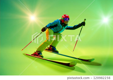Side view, low angle of athletic woman, skier gliding forward against intense green studio background in neon green ambiance. 120982238