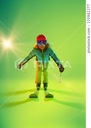 Front view, dynamic photo of skier bends into aerodynamic pose, skis parallel, and poles outstretched in neon light against studio background. Front view, dynamic photo of skier bends into aerodynamic pose, skis parallel, and poles outstretched in neon light against studio background. 120982277