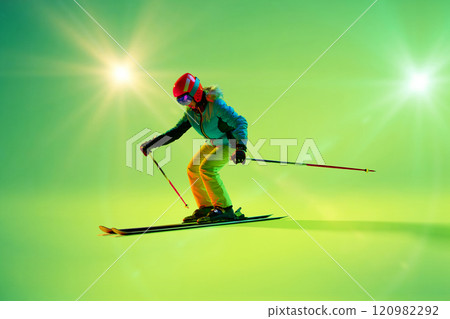 Athletic woman, kier bends into sharp turn against glowing green backdrop. Colorful illumination enhances action's energy. 120982292