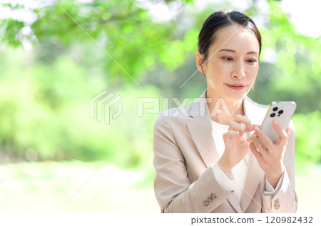 A businesswoman using her smartphone while sitting on a park bench 120982432