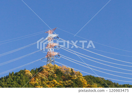 Power lines running through the mountains and a power transmission tower shining in the setting sun 120983475