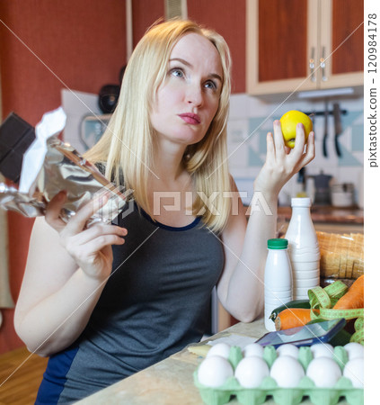 A woman checks the calorie content of food in a smartphone app. Calorie counting for weight loss. There are products for dieting on the table A woman checks the calorie content of food in a smartphone app. Calorie counting for weight loss. There are products for dieting on the table 120984178