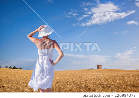 Woman holding hat in grain field in Provence, France Woman holding hat in grain field in Provence, France 120984372