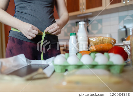 A woman checks her belly circumference with a measuring tape. There are diet foods on the table. Healthy lifestyle and weight loss A woman checks her belly circumference with a measuring tape. There are diet foods on the table. Healthy lifestyle and weight loss 120984528