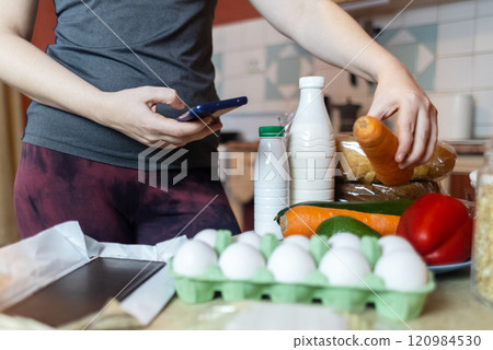 A woman checks the calorie content of food in a smartphone app. Calorie counting for weight loss. There are products for dieting on the table A woman checks the calorie content of food in a smartphone app. Calorie counting for weight loss. There are products for dieting on the table 120984530
