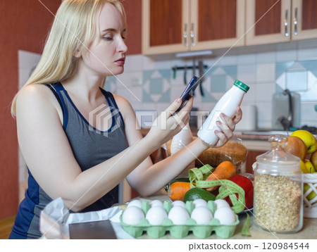 A woman checks the calorie content of food in a smartphone app. Calorie counting for weight loss. There are products for dieting on the table A woman checks the calorie content of food in a smartphone app. Calorie counting for weight loss. There are products for dieting on the table 120984544