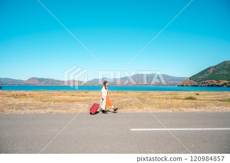 Women's trip: A young woman walking under the blue sky with a carry bag Women's trip: A young woman walking under the blue sky with a carry bag 120984857