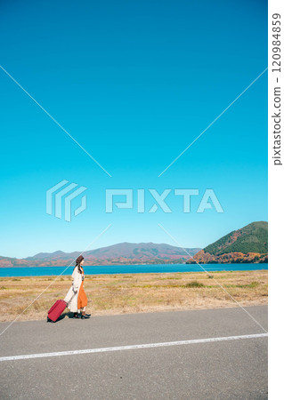 Women's trip: A young woman walking under the blue sky with a carry bag 120984859