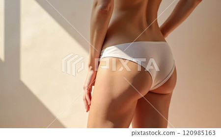 Minimalist artistic portrait of a woman's lower back and legs in neutral underwear, emphasizing skin tone and curves. 120985163