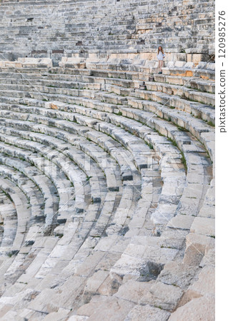 A young woman walk by ancient ruins in Patara, Turkey. Girl look at ruined amphitheater. History and adventure. This scenic archaeological site offers breathtaking view, perfect for cultural tourism. 120985276