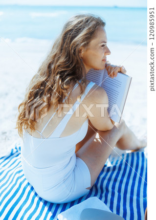 relaxed modern woman on ocean shore with straw bag and book 120985951