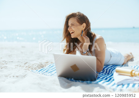 happy elegant woman on beach using laptop 120985952