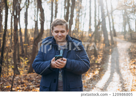 Adult 30s man hiker stand outdoors in a natural setting, smile while using his mobile phone outdoors. Hiking, lifestyle, adventure and tourism concept. 120986805