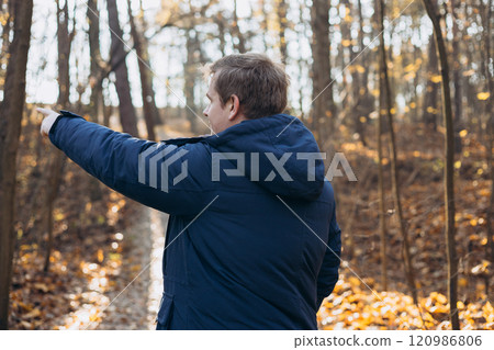 One Caucasian male hiking in the woods in autumn. Travel, active lifestyle, people and hobby concept. Blonde male in sport clothes pointing finger outdoors. Traveler enjoys eco-tourism, rear view 120986806