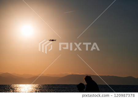 A silhouette of a man flying a drone at dawn, a scenic shot of sunrise over the sea.  120987378