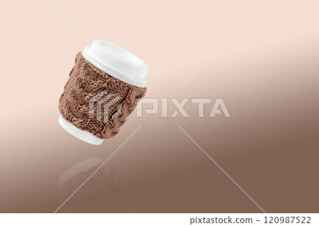 Cup made of cardboard for takeaway coffee with knitted cover and white lid. Concept of takeaway coffee, walking, energetic life. Demonstrating the colors of 2025 - Mocha Mousse. Cup made of cardboard for takeaway coffee with knitted cover and white lid. Concept of takeaway coffee, walking, energetic life. Demonstrating the colors of 2025 - Mocha Mousse. 120987522