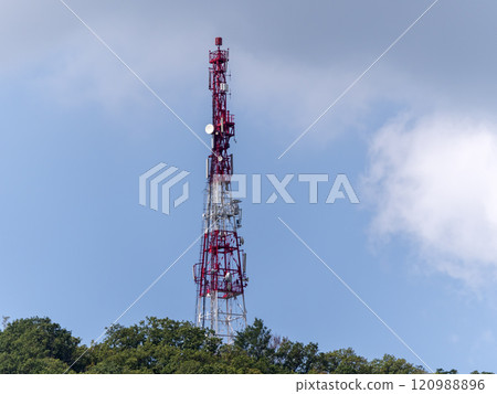 Directional antenna array on a red and white communication tower against sky 120988896