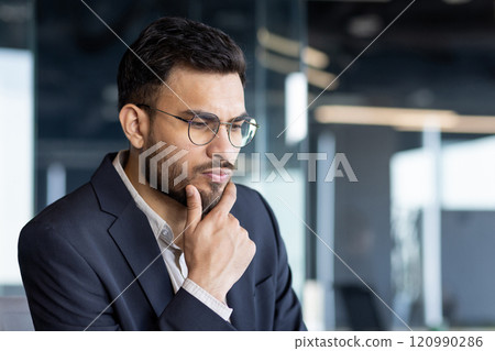 A thoughtful businessman in a suit, deep in contemplation, reflects serious decision-making in a modern office setting. This image captures professional focus and critical thinking. 120990286