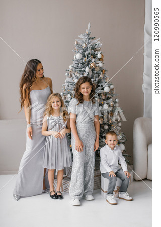 Happy family of four posing in front of Christmas tree. Mother is wearing long dress and the children are wearing sparkly outfits Happy family of four posing in front of Christmas tree. Mother is wearing long dress and the children are wearing sparkly outfits 120990565