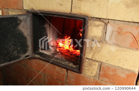 Smoldering burning coals in an open brick oven. Black soot on the walls of the oven and on the door. Heat from the burning fire. Traditional heating system in the house. Smoldering burning coals in an open brick oven. Black soot on the walls of the oven and on the door. Heat from the burning fire. Traditional heating system in the house. 120990644